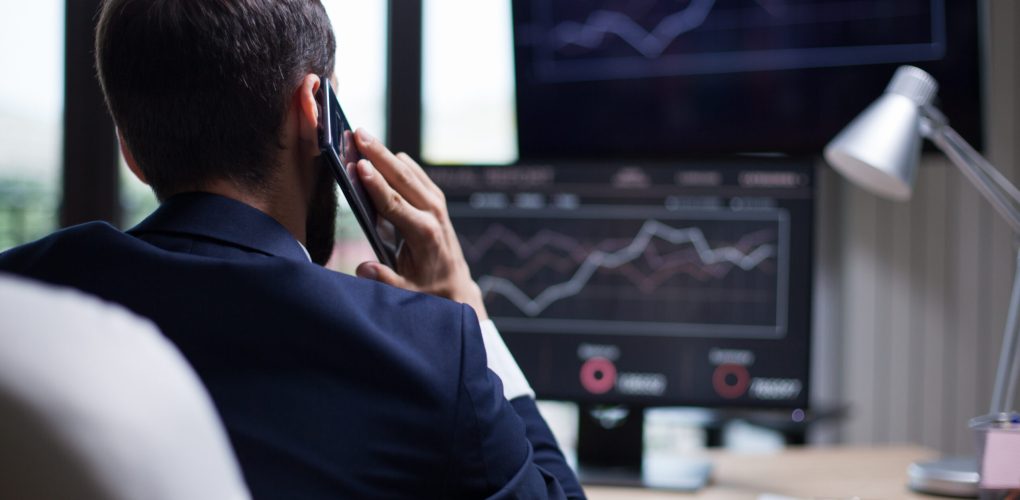 Back view of young business bearded man having a phone call with his CEO. Diagrams on computer monitor.