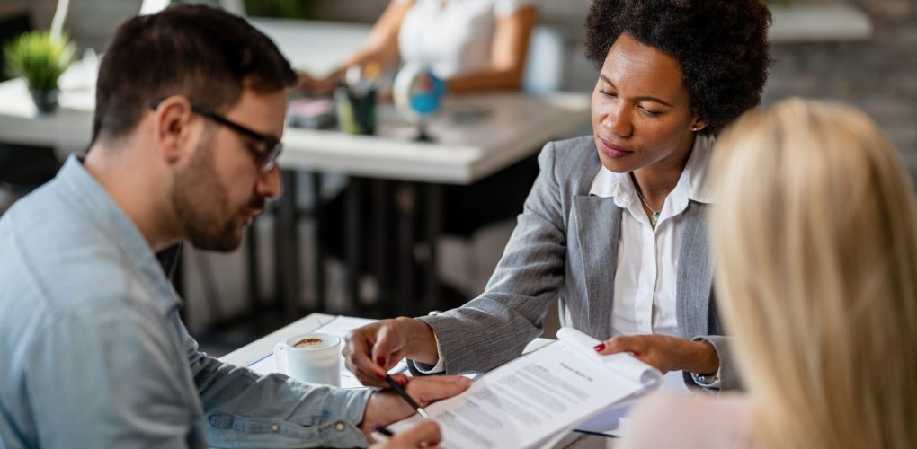 Black female real estate agent showing to a couple where to sign the contract during the meeting in the office.