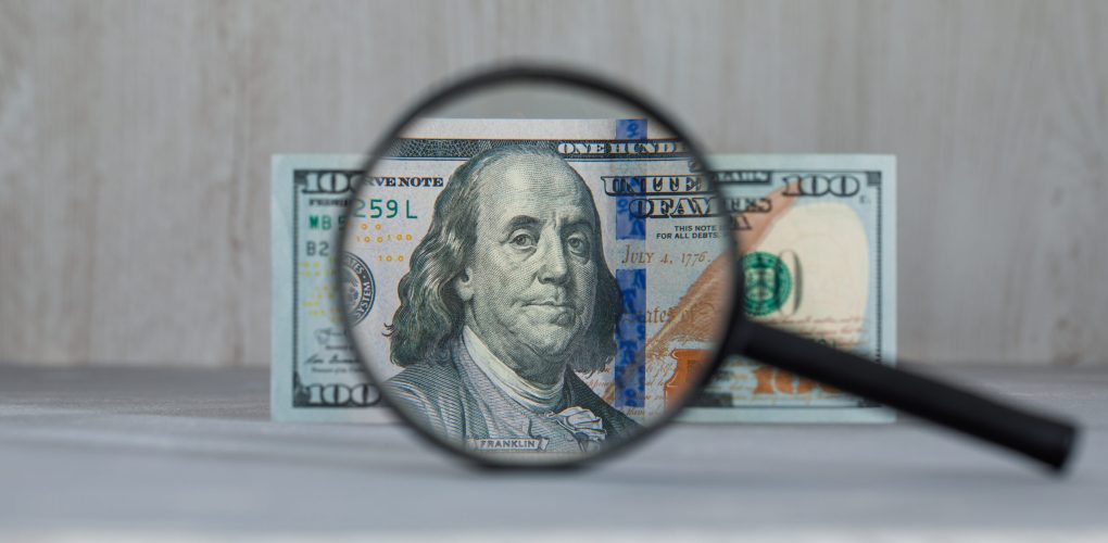Business and monetary concept with magnifying glass over dollar banknote on grey and wooden background side view.